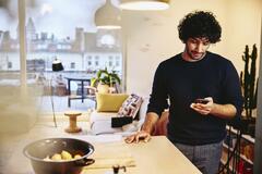 Man standing next to the kitchen counter top, looking at his phone.