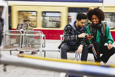 Man and woman looking at phone while sitting on a bench on a train platform.